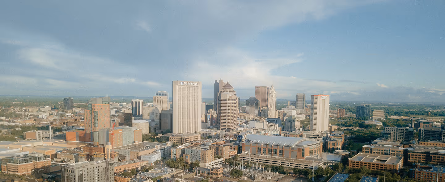 Panoramic view of a city skyline with tall buildings under a partly cloudy blue sky.