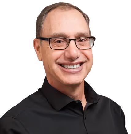 Smiling middle-aged man with short brown hair and glasses wearing a black collared shirt.