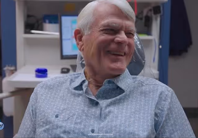 Smiling elderly man with white hair sitting in a dental chair in a clinic.