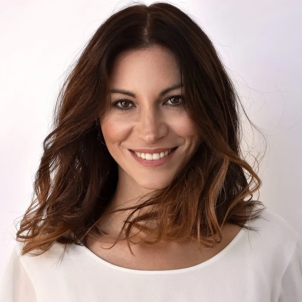 Porträt von dr. dr. Maja Grahovac (Führende Fachärztin für Haut- und Geschlechtskrankheiten) mit langen braunen Haaren und weißem Oberteil, die lächelt.