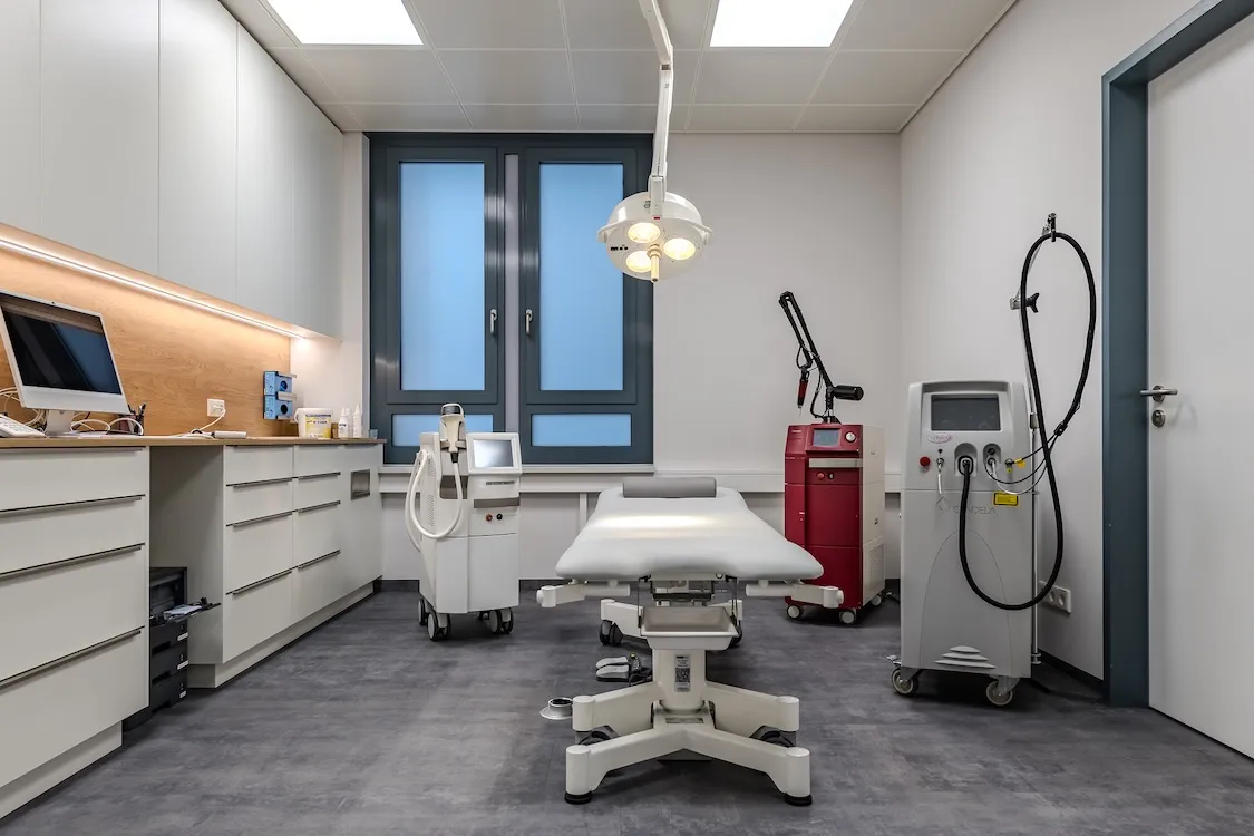 Moderne Klinik mit Behandlungsliege, medizinischen Geräten und einem Computer am Tisch.