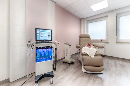 Moderne Behandlungszimmer mit medizinischem Gerät und einem bequemen Behandlungssessel vor zwei Fenstern mit Jalousien.