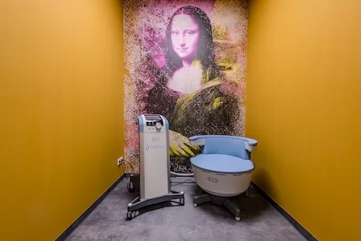 Ein moderner Raum mit gelben Wänden, der eine Maschine und einen Stuhl vor einer Wand mit einem großen Bild der Mona Lisa zeigt.