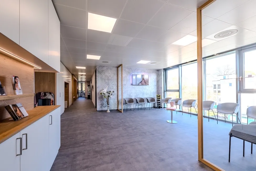 Moderne, helle Wartezimmer mit Stühlen entlang der großen Fensterfront und einem Couchtisch in der Mitte.