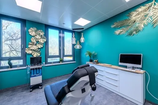 Moderner Behandlungsraum mit einem Zahnarztstuhl, hellen Fenstern und türkisfarbenen Wänden, dekoriert mit Pflanzen und Wandkunst.
