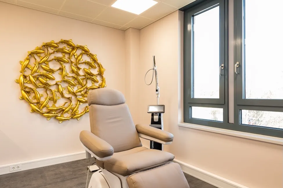 Moderne medizinische Behandlungsliege vor einem Fenster mit goldfarbenem Wanddekor aus Fischen.