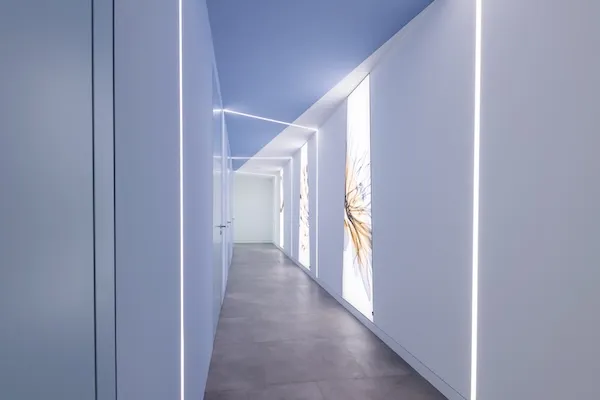 Moderner, weißer Flur mit integrierter LED-Beleuchtung und beleuchteten Wandpaneelen mit abstrakten Designs.