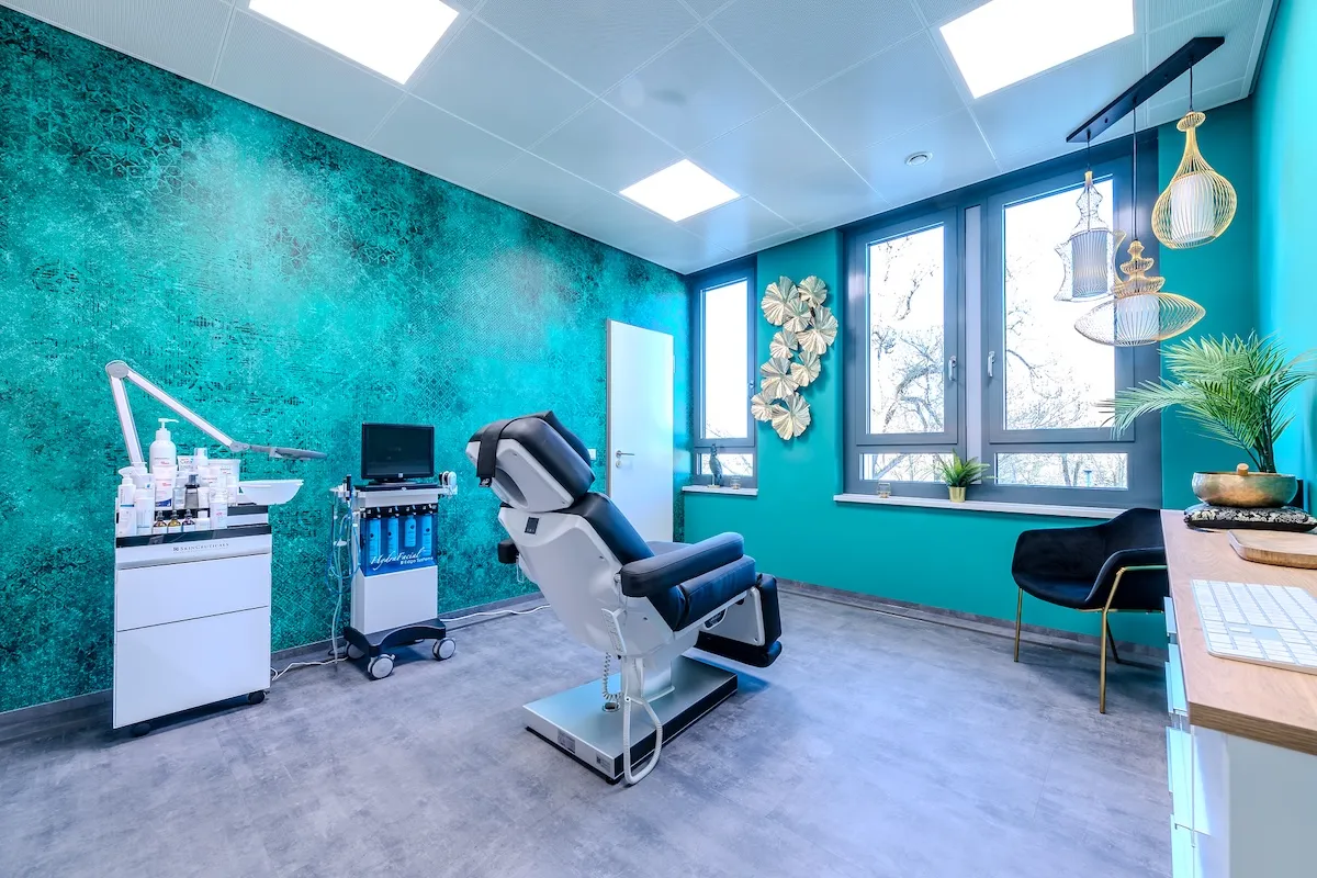 Behandlungszimmer mit blauer Wand, medizinischem Stuhl, Geräten und Dekoration in der Praxis.