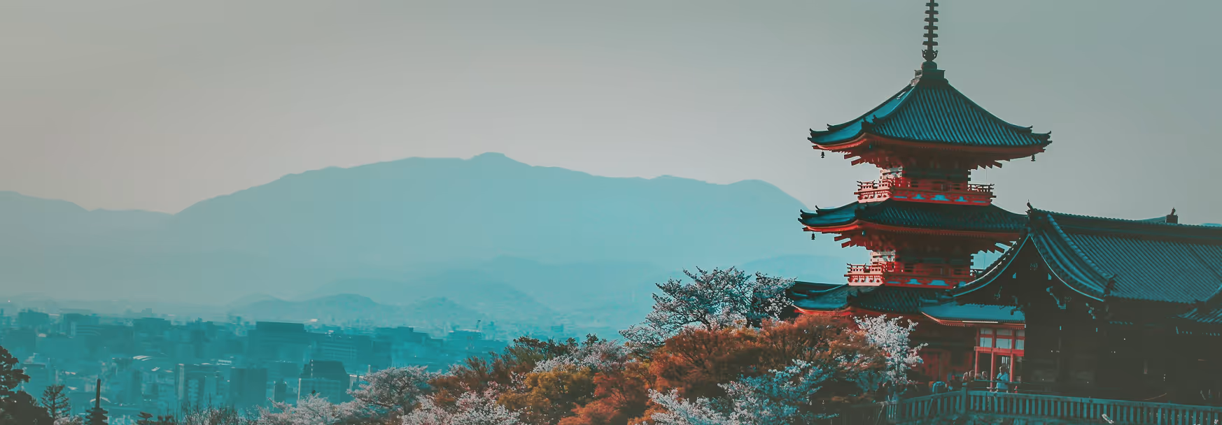 Traditional Japanese pagoda among trees with a city and mountains in the background.