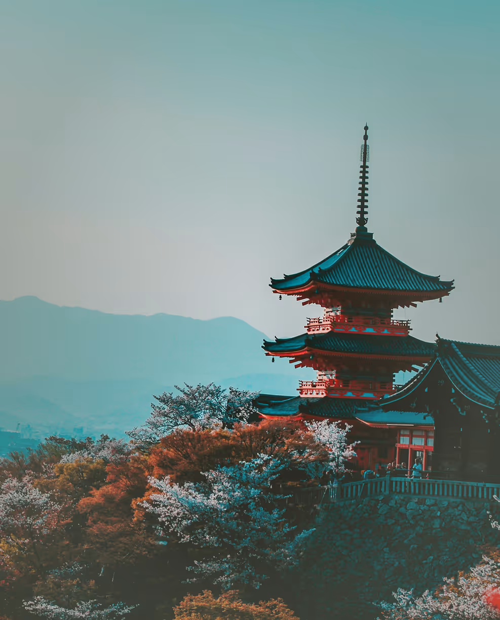 Traditional Japanese pagoda surrounded by blooming cherry blossoms with mountain backdrop.