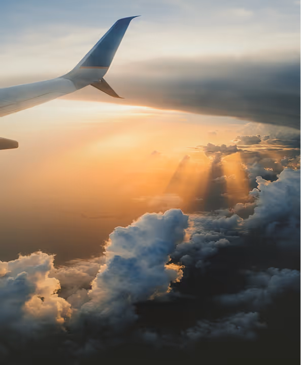 Airplane wing above clouds with sunlight rays breaking through at sunset.