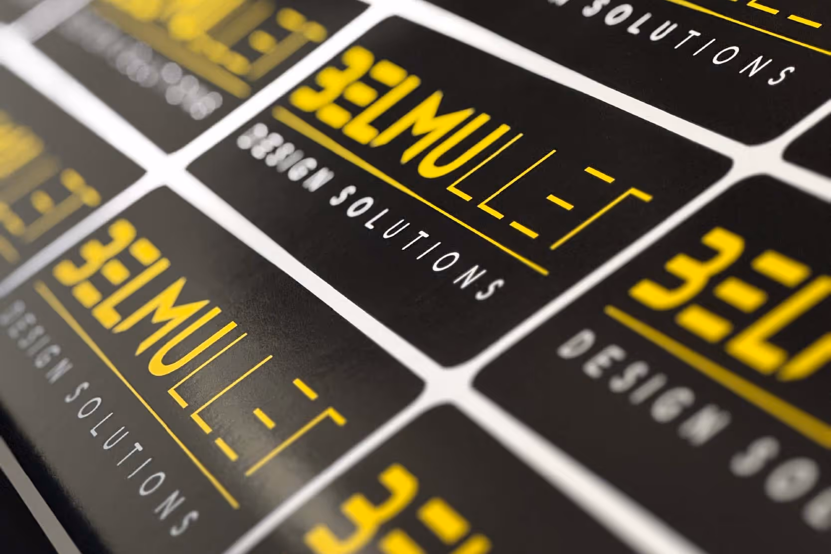 Close-up of mass produced premium vinyl stickers with yellow and white text reading Bell Mullet Design Solutions