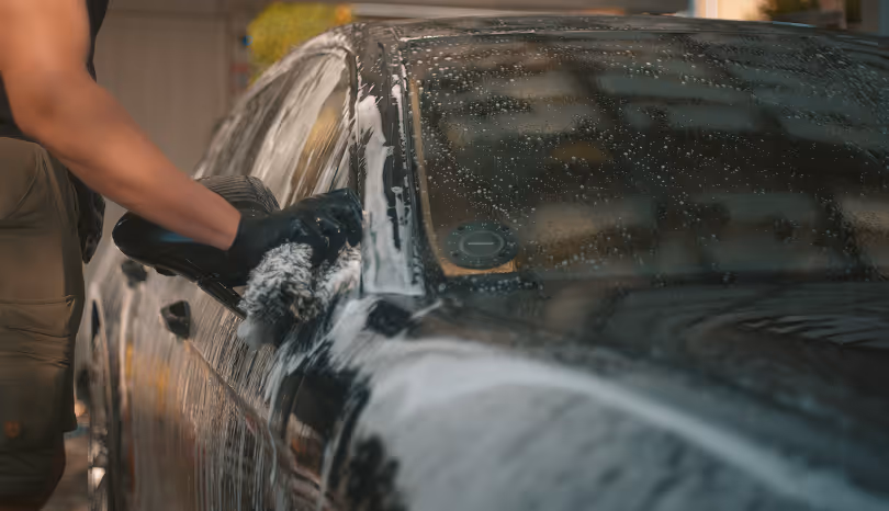 Person med sorte handsker vasker en sort bil med sæbeskum ved hjælp af en børste