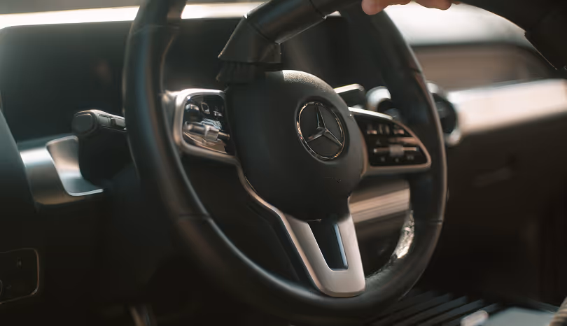 Person der rengør et sort Mercedes-Benz rattet med en støvsuger inde i en bil