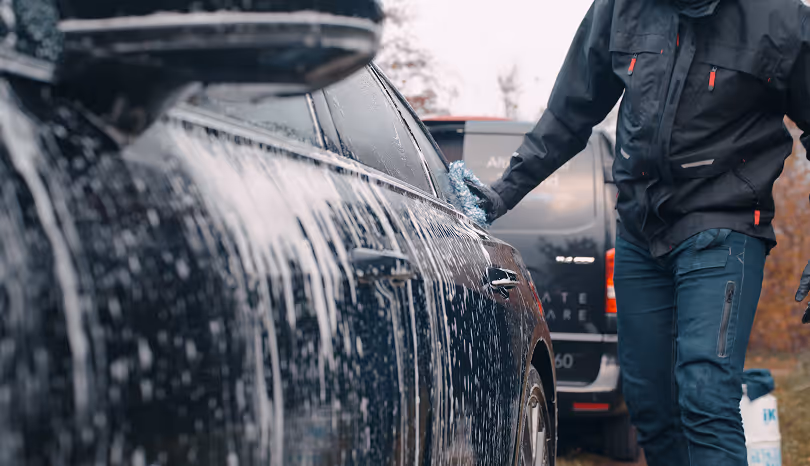 Person der vasker en sort bil dækket af sæbeskum udendørs