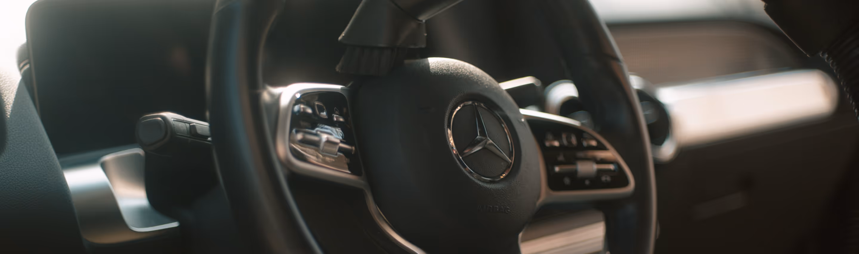 Nærbillede af et Mercedes-Benz bil rattet med kontrolknapper og logo i fokus