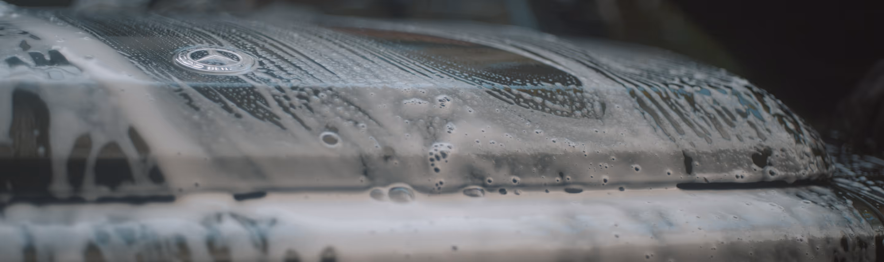 Nærbillede af en sort Mercedes bil motorhjelm dækket af sæbeskum under vask