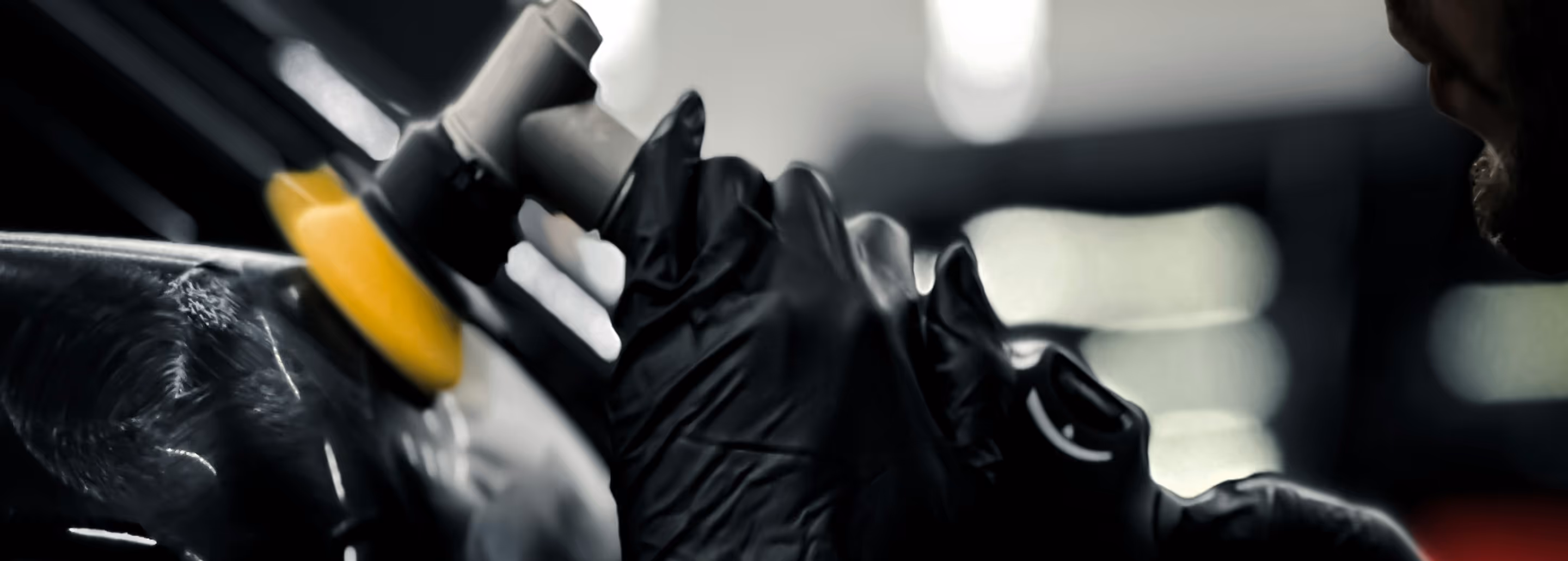 Person med sorte handsker polerer en mørk biloverflade med en polermaskine