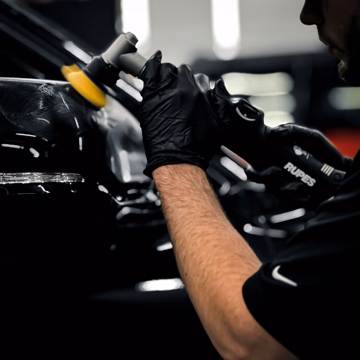 Person med sorte handsker bruger en Rupes polermaskine på en sort biloverflade