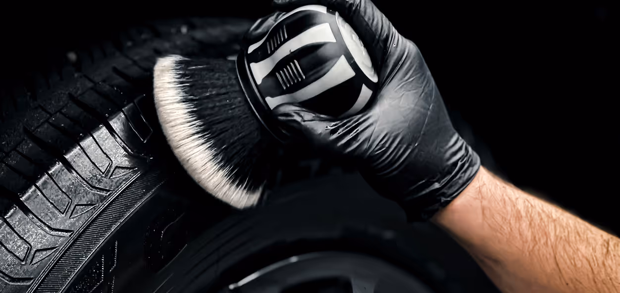 Hånd i sort handske, der rengør et bildæk med en cirkulær børste.