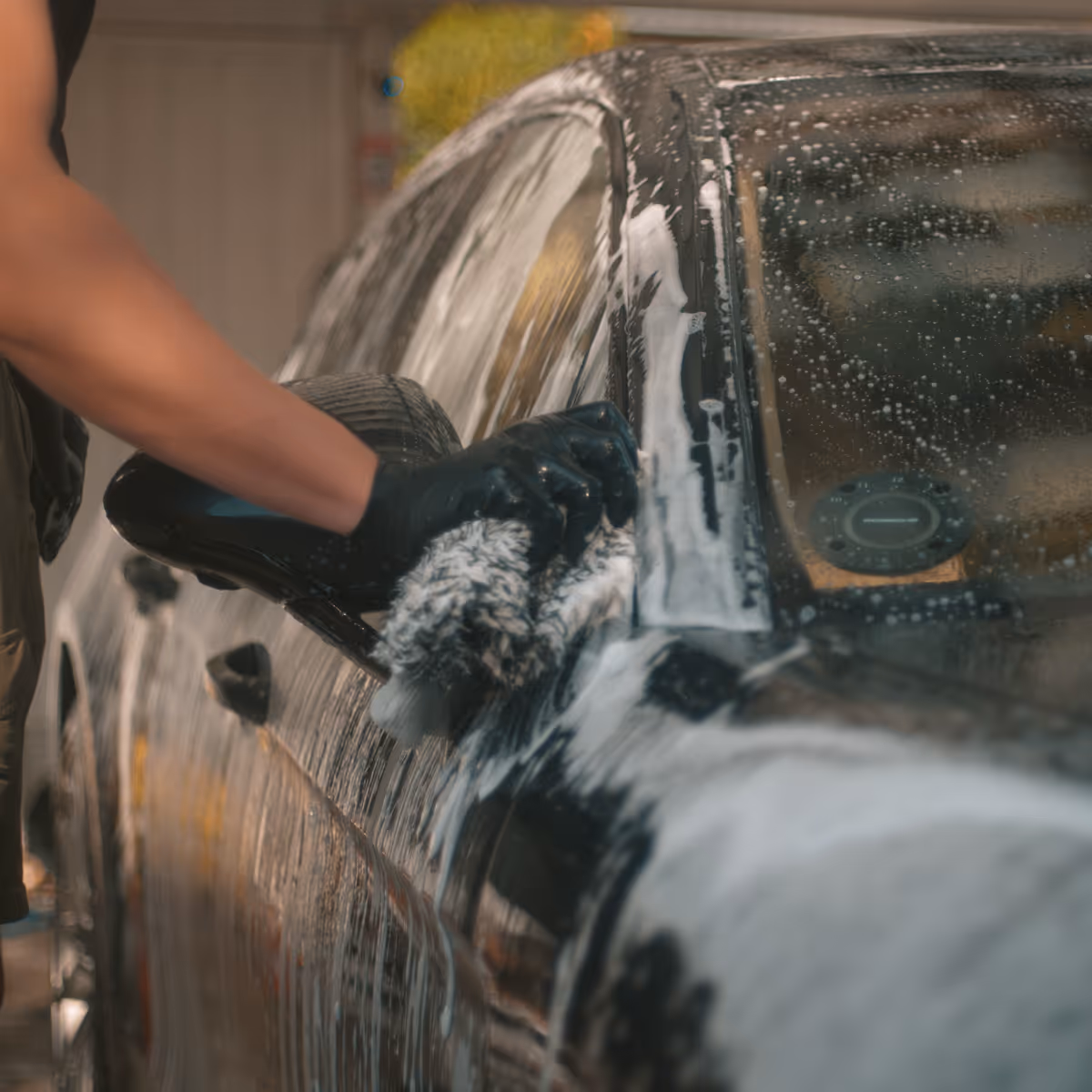 Person med sorte handsker der vasker en sort bil med en sæbevåd svamp