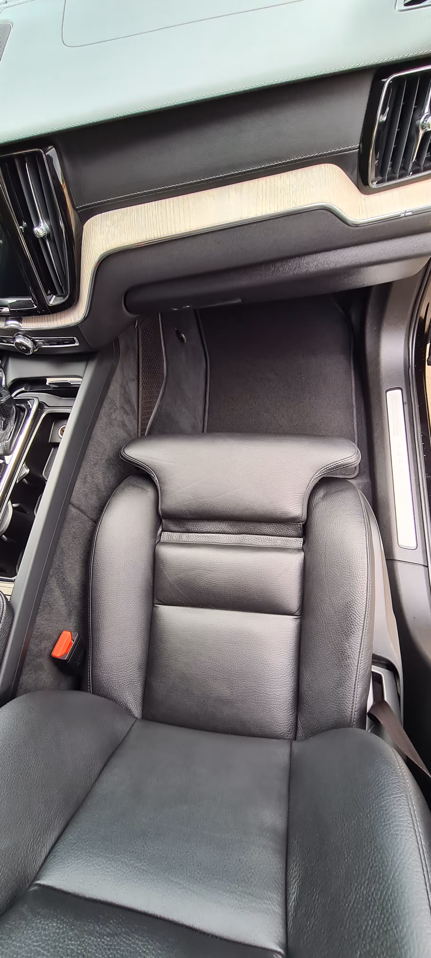 Sort læder passagersæde og gulvområde inde i en bil med lys trætrim på instrumentbrættet og en gearstang til venstre