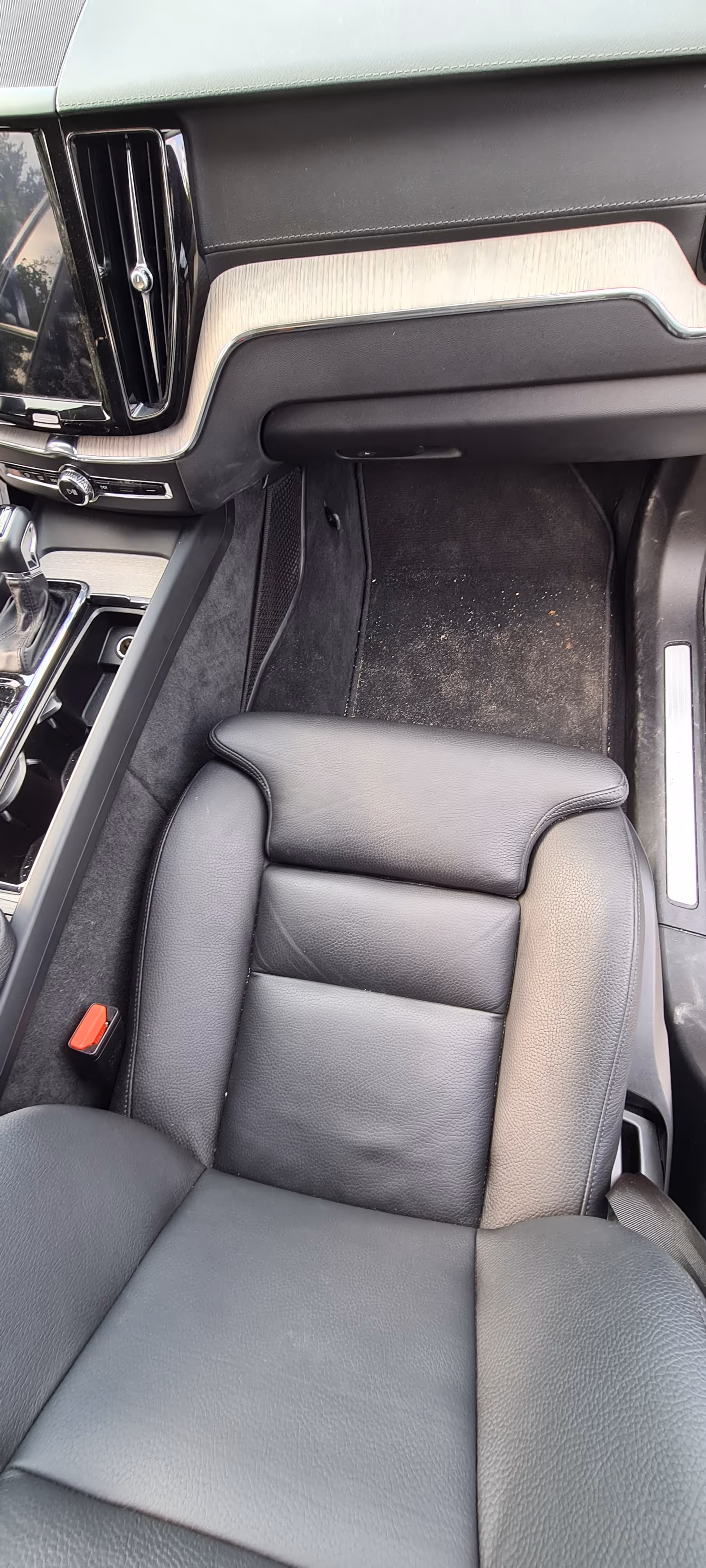 Beskidt sort læder passagersæde og gulvområde inde i en bil med lys trætrim på instrumentbrættet og en gearstang til venstre