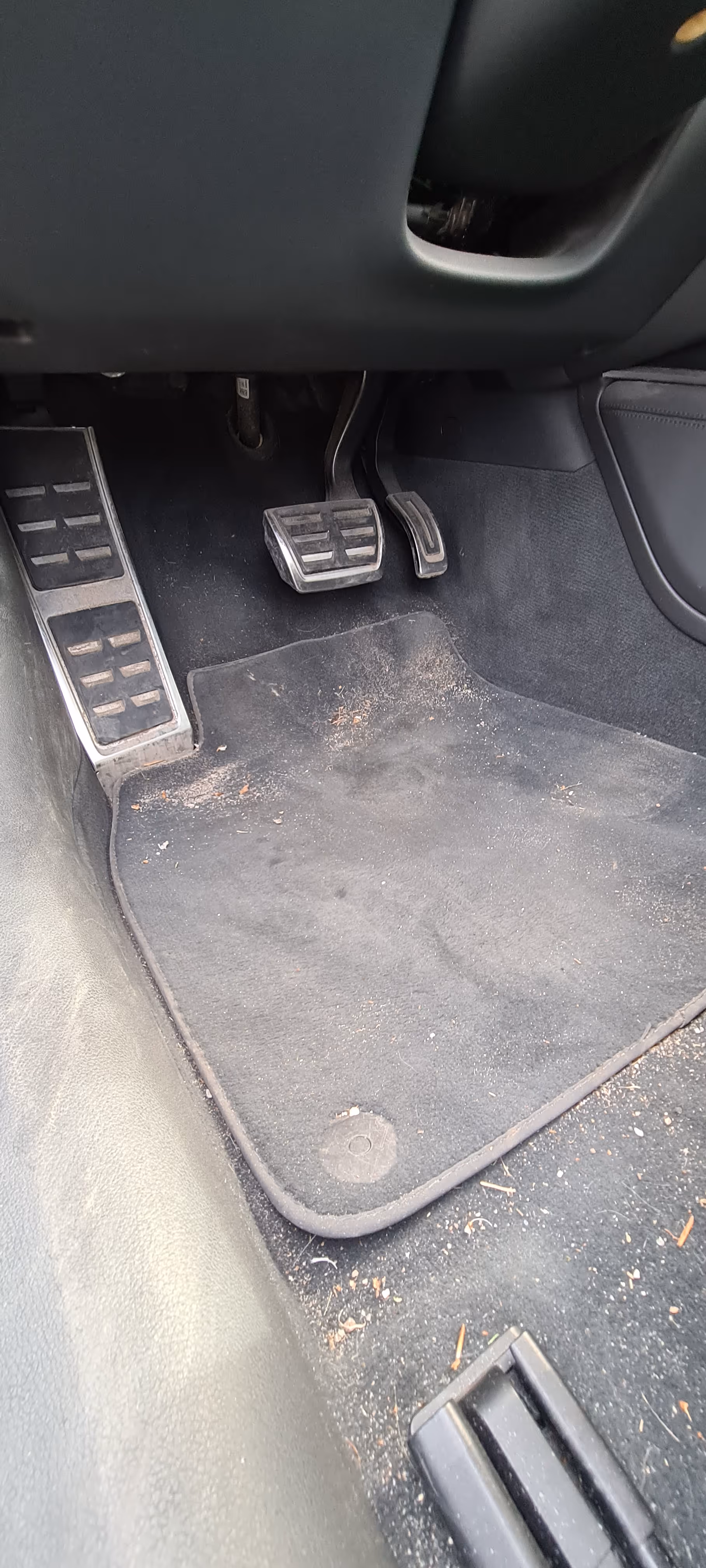 Førersidens fodrum i en manuel bil med kobling, bremse og speeder pedaler med et let beskidt sort gulvtæppe