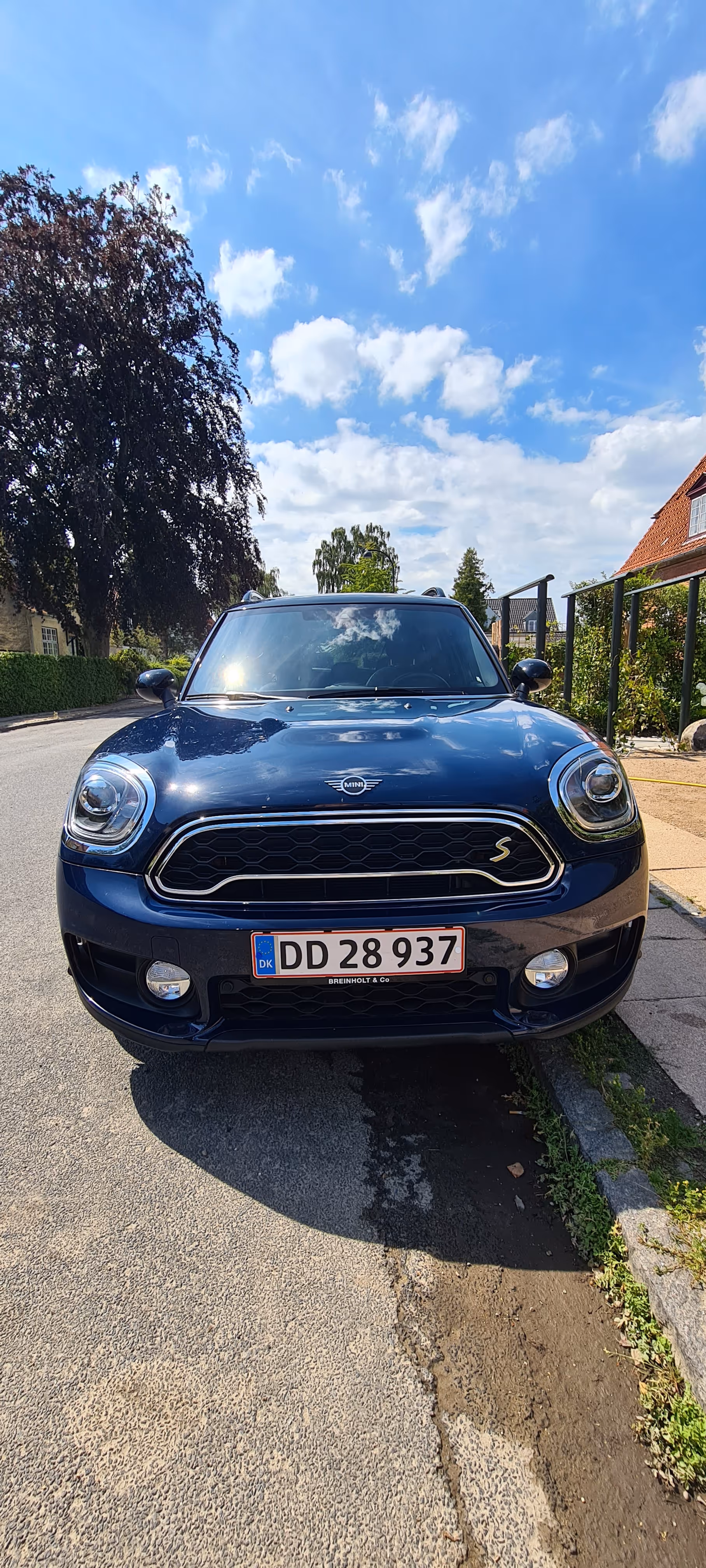Frontvisning af en blå Mini Cooper S parkeret på en gade under en delvist overskyet himmel