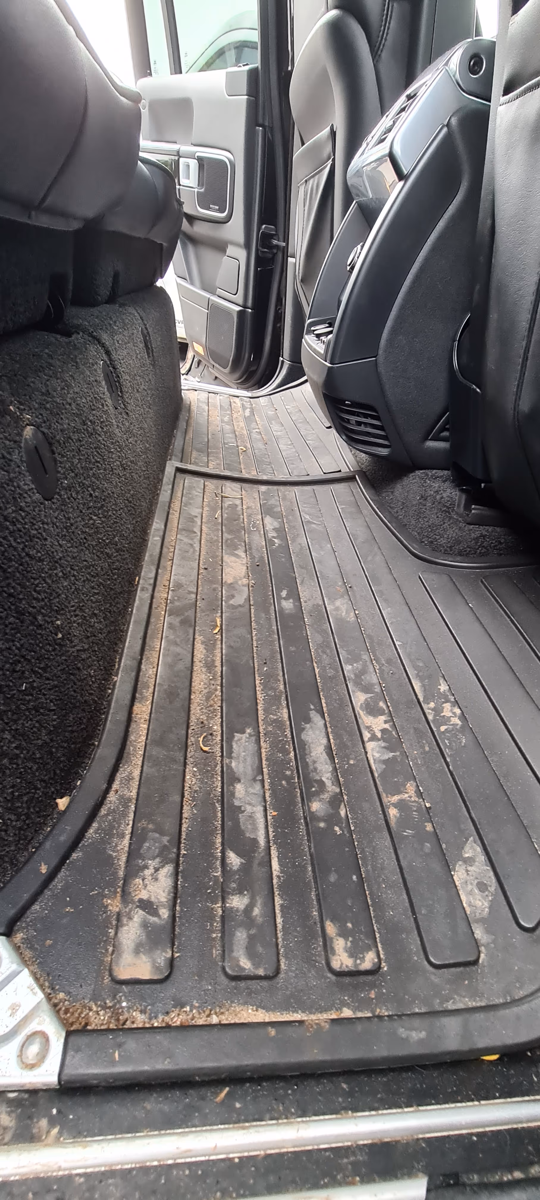 Beskidte sorte gummi-gulvtæpper, der dækker gulvet på bagsædet i en bil med åben dør og sorte lædersæder