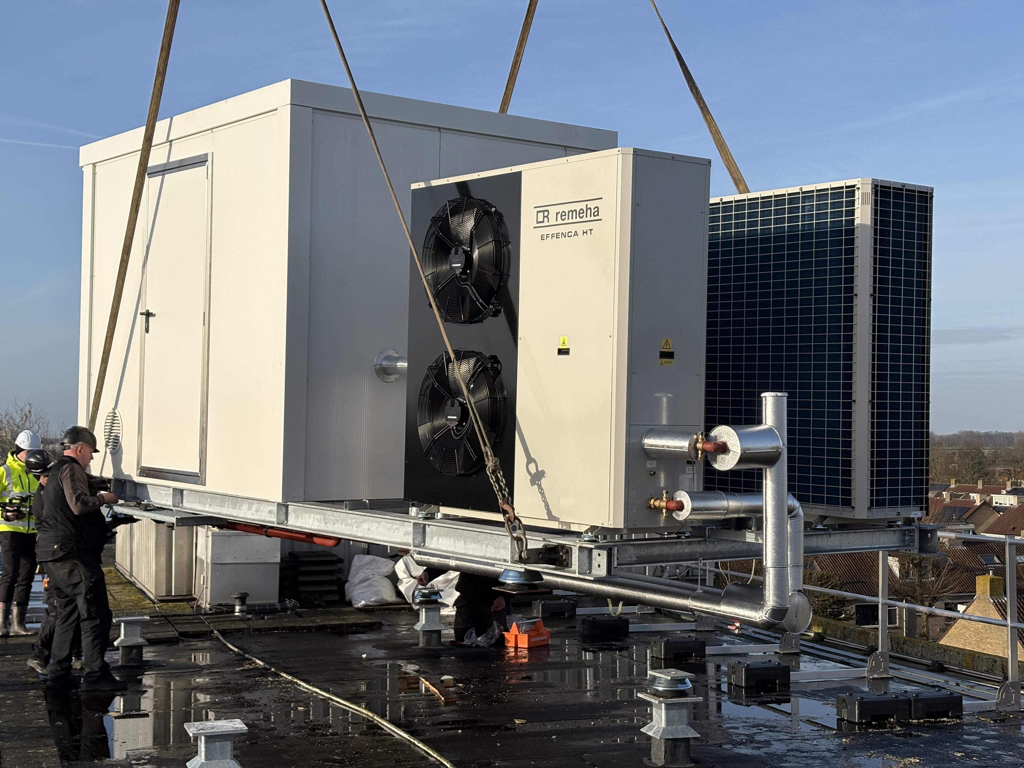 Technici installeren een grote Remeha Effenca HT HVAC-eenheid op een dakterras met zicht op de stad.