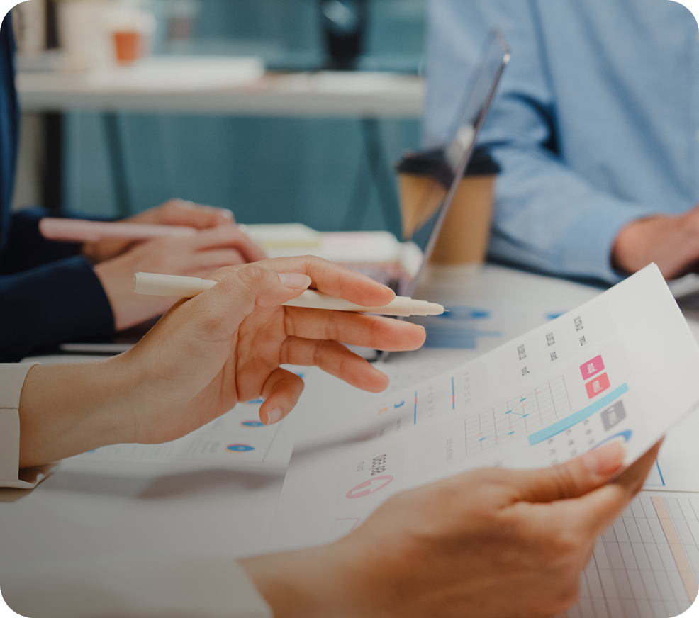 Three colleagues at a conference table reviewing a printed report of health analytics charts, one holding a pen