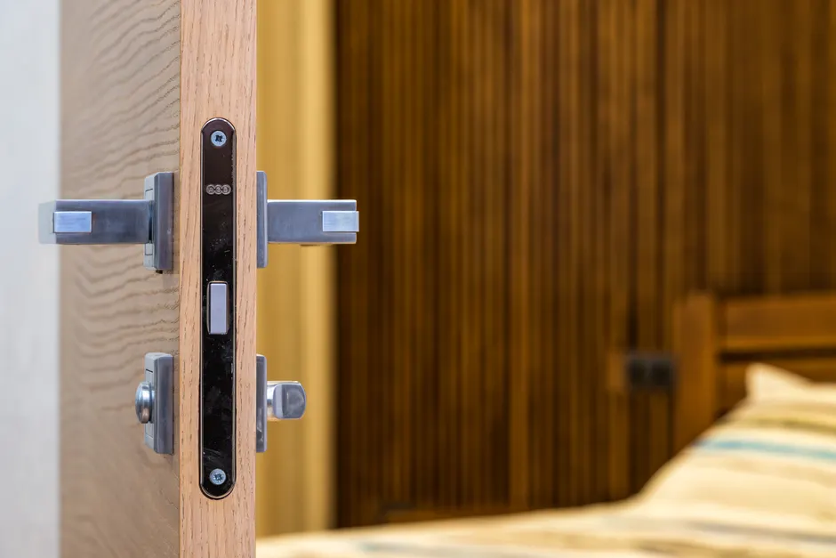 Serrure et poignée sur le montant d'une porte en bois, chambre en arrière-plan