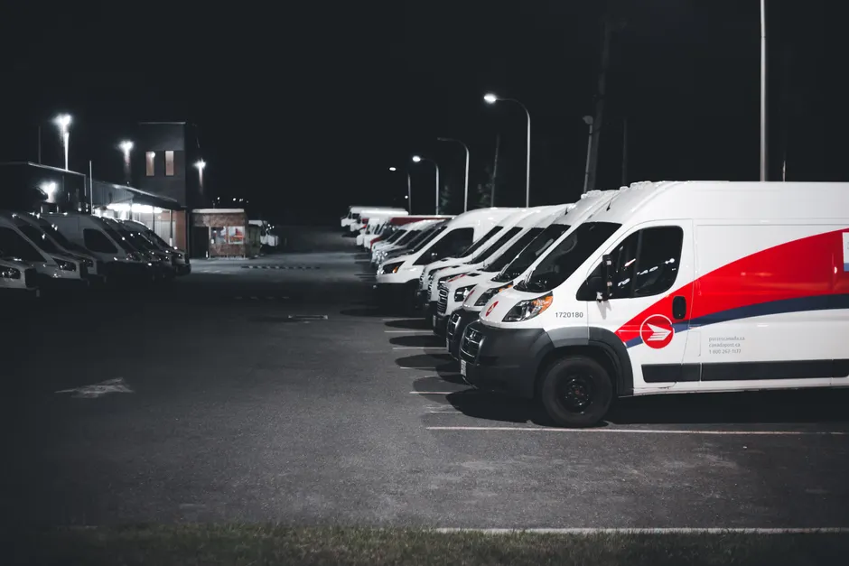 Flotte d'utilitaires blancs alignés sur un parking éclairé de nuit