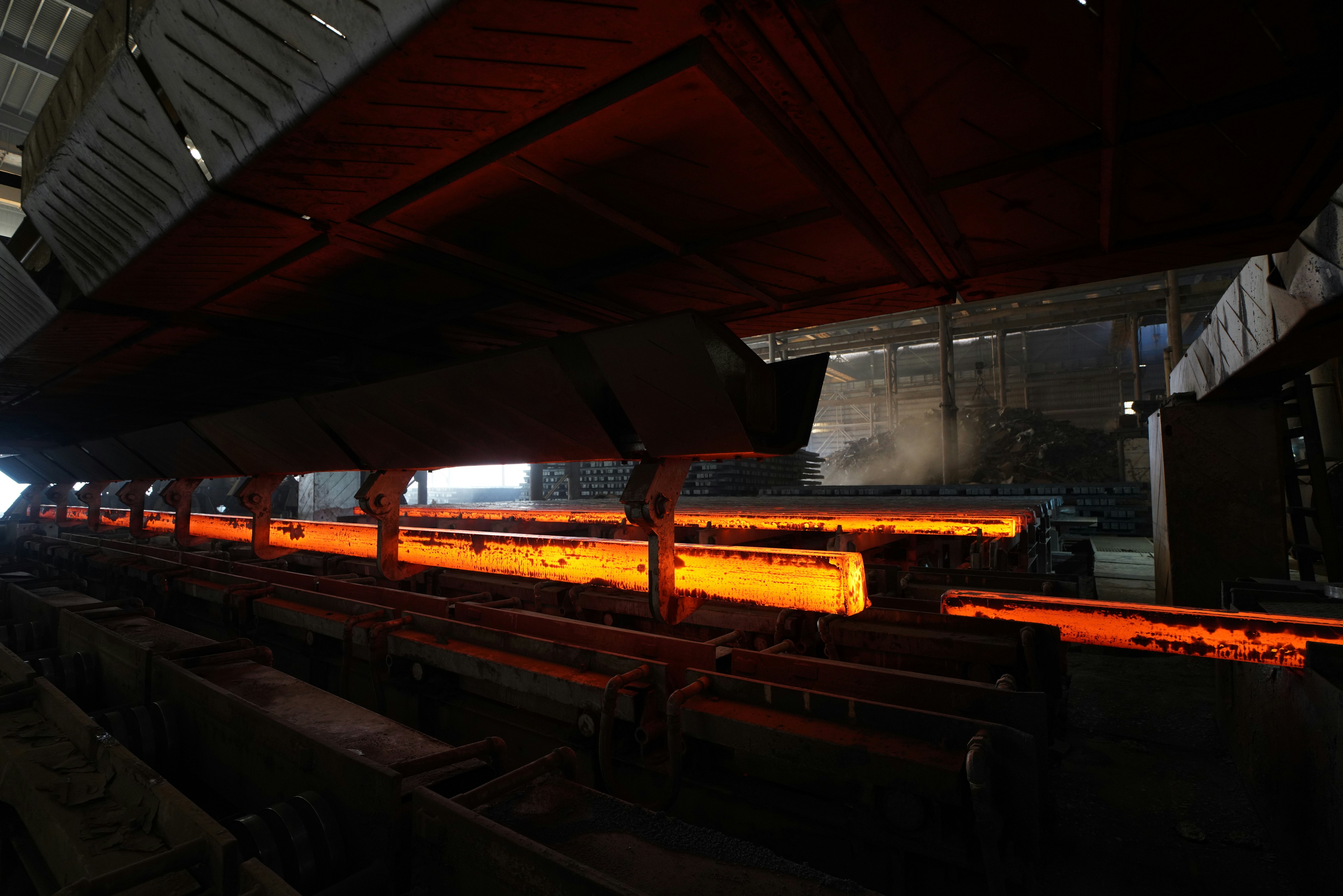 Glowing hot steel beams being processed in an industrial steel mill.