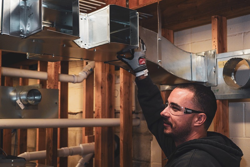 Worker wearing safety glasses and glove installing metal ductwork in a building under construction.