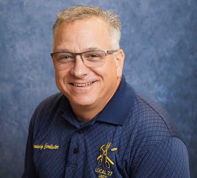 Smiling middle-aged man with glasses wearing a navy blue shirt with Local 27 JATC logo.