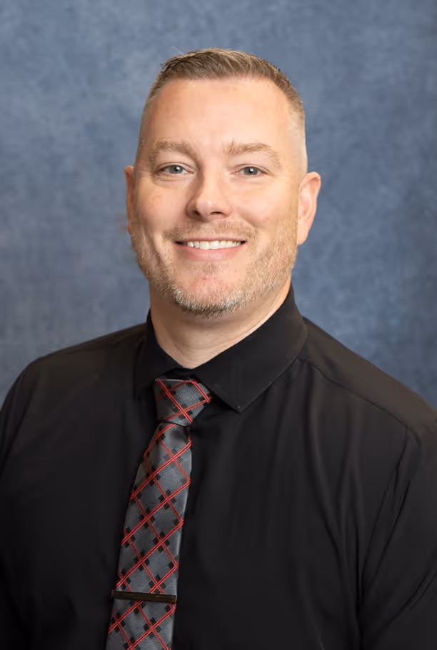 Smiling man with short hair and trimmed beard wearing a black shirt and patterned tie.