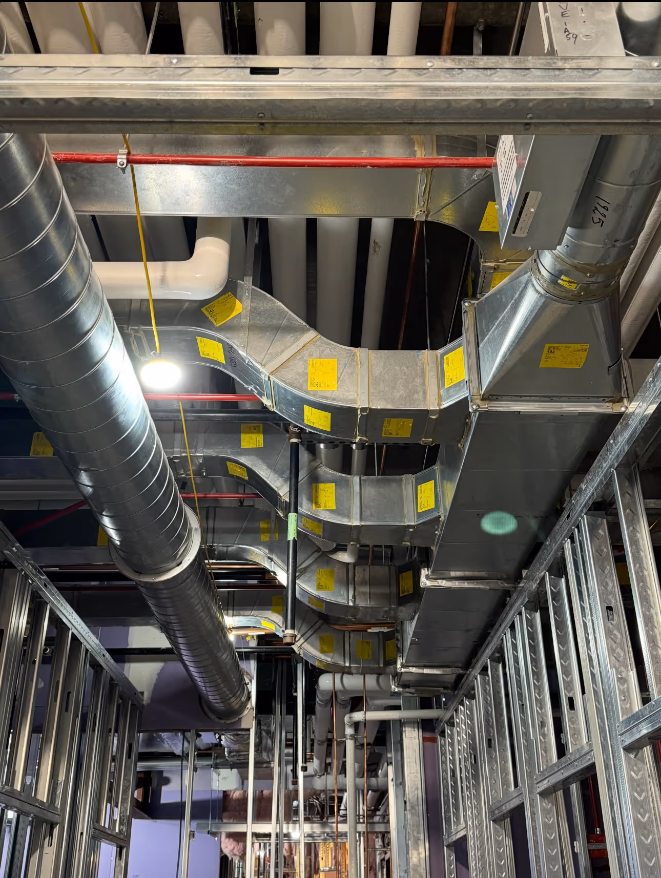 Metal ductwork and pipes installed in an industrial or commercial building ceiling framework.