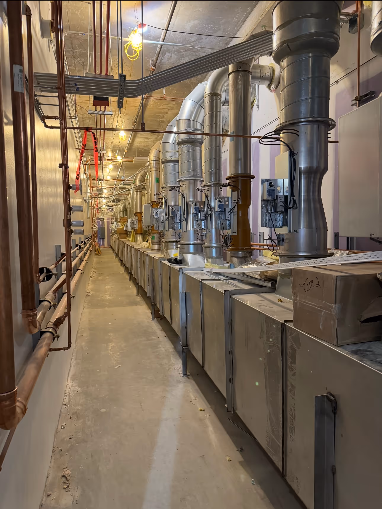 Long industrial corridor with ventilation ducts and piping along the ceiling and walls.
