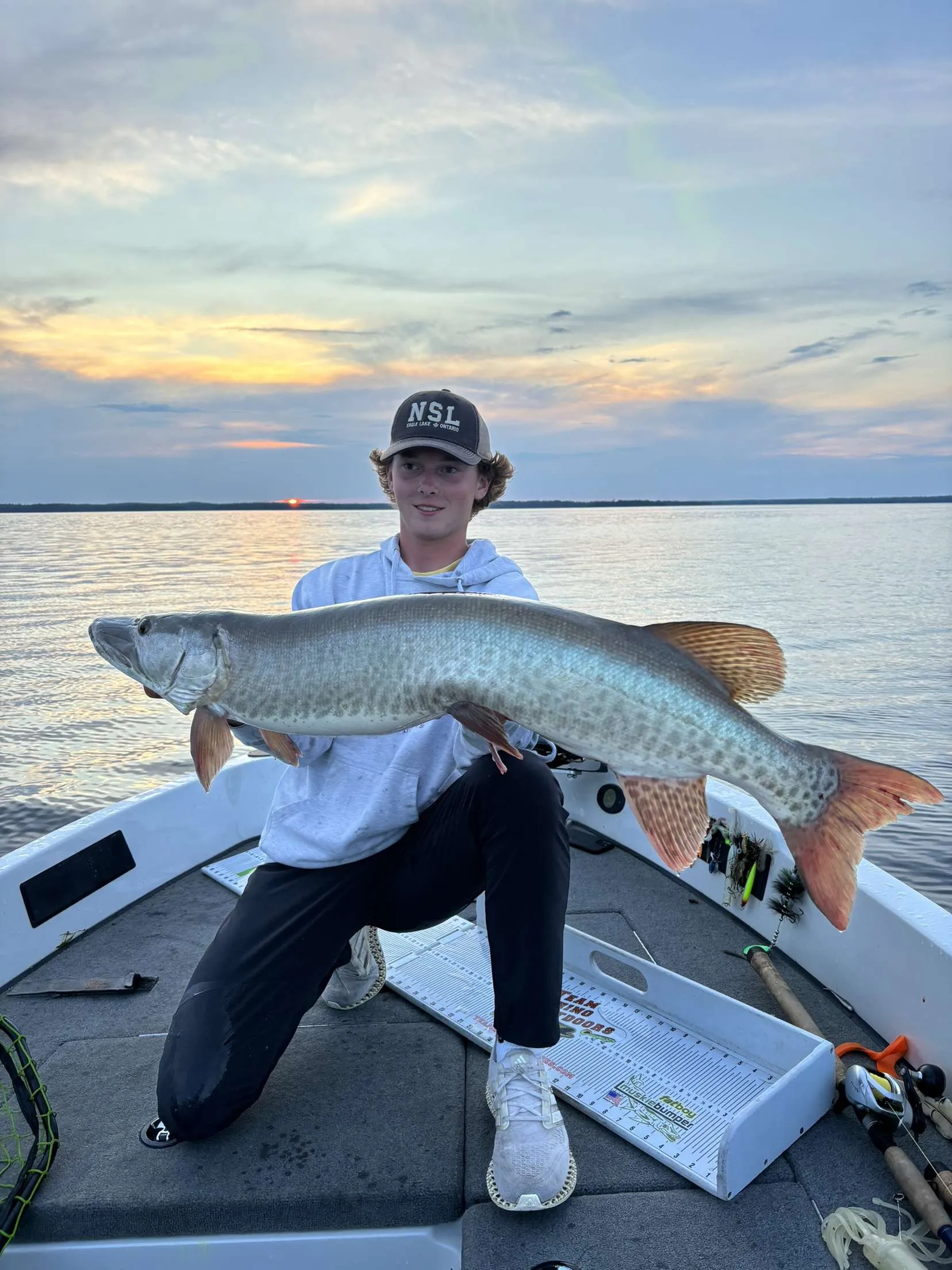 Young angler kneeling in a boat with a musky at sunset