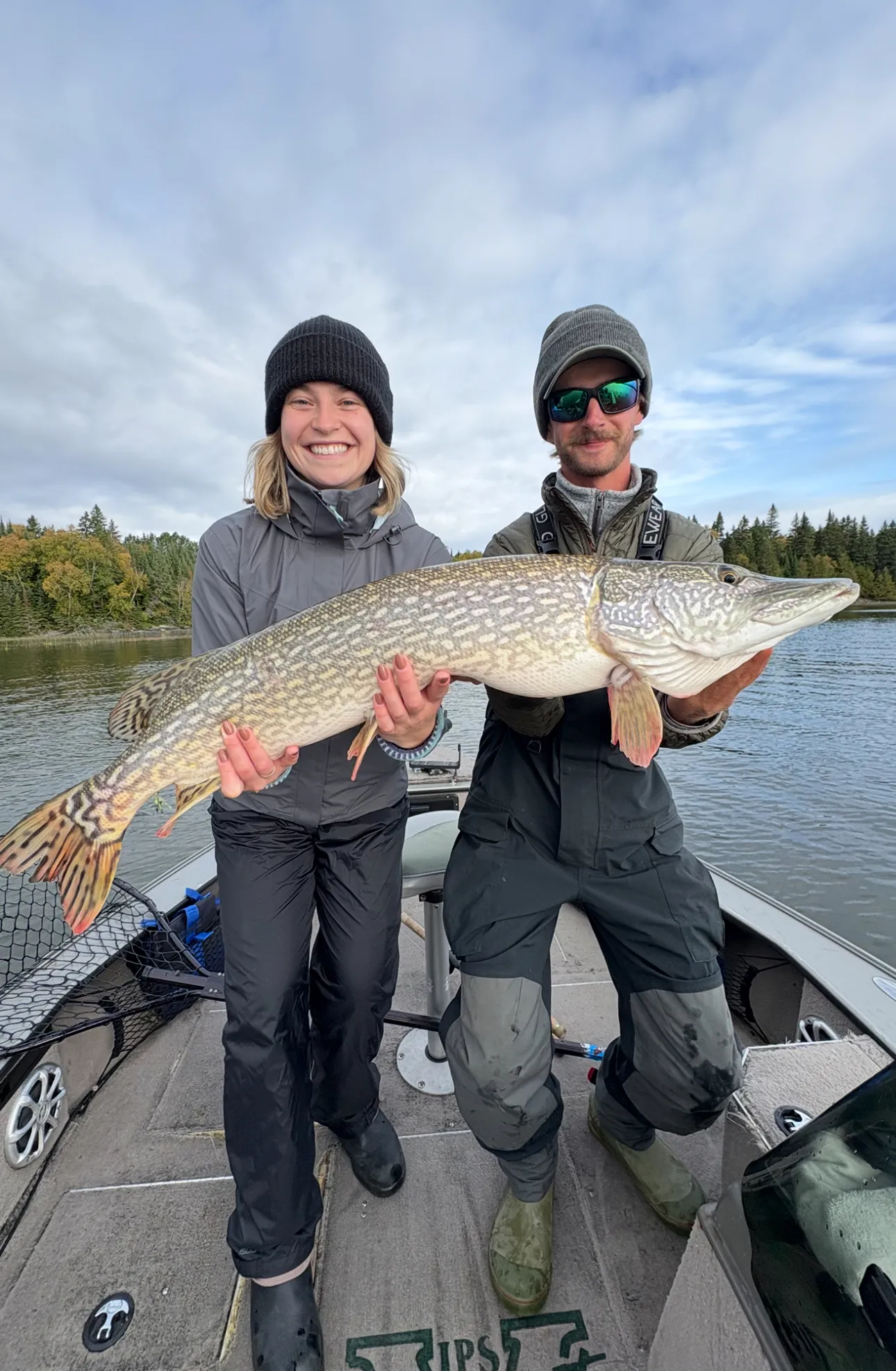 Two anglers holding a northern pike in a boat
