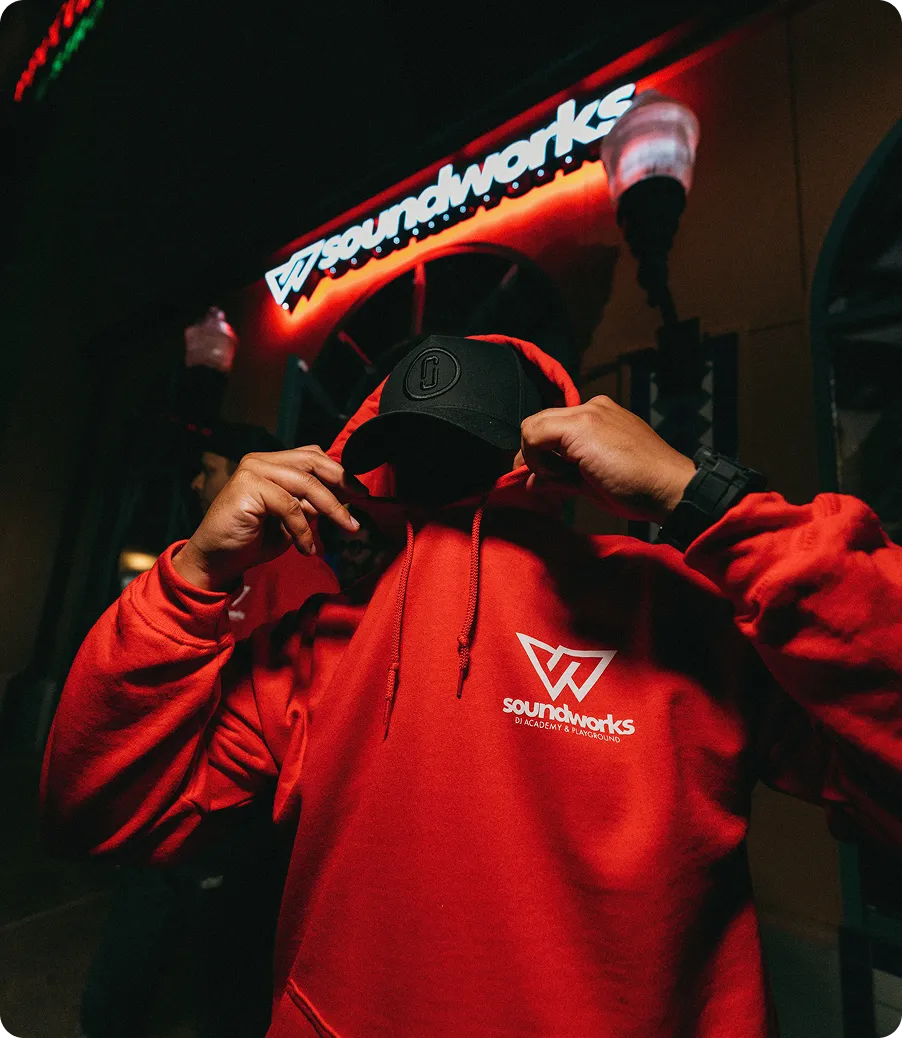 Person wearing a red Soundworks hoodie adjusting a cap outside the studio at night