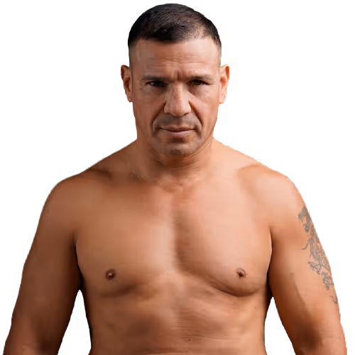 Muscular shirtless man with short hair and a tattoo on his left arm, looking forward with a serious expression.