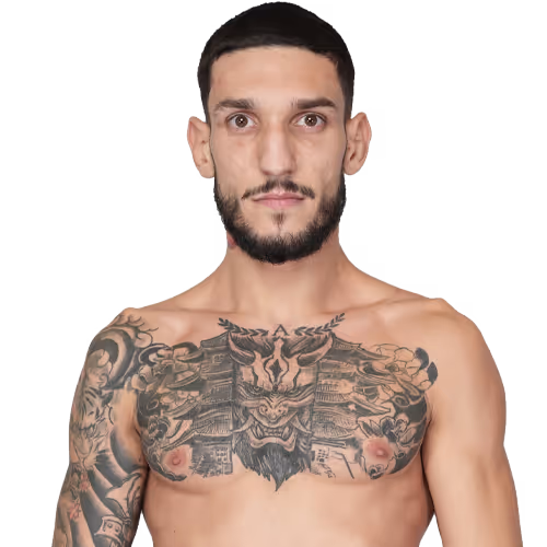 Shirtless man with a beard and short hair showing chest and arm tattoos, including a large intricate design on his chest.