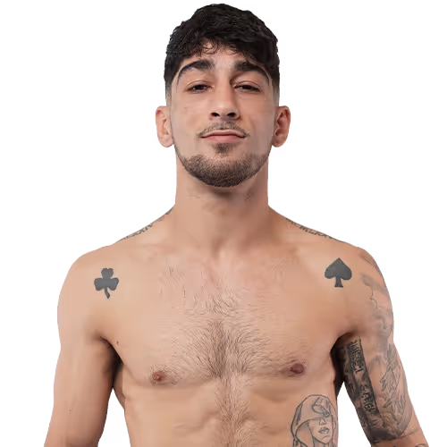 Shirtless young man with short dark hair, showing tattoos of a club and spade on his shoulders and a woman's face on his left arm.