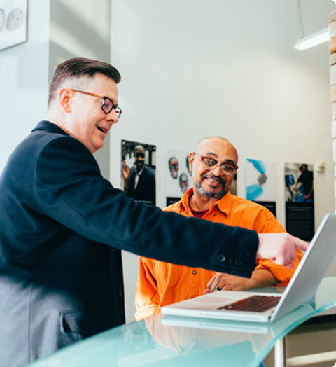 Two people standing at a counter, discussing and pointing at a laptop in a bright office