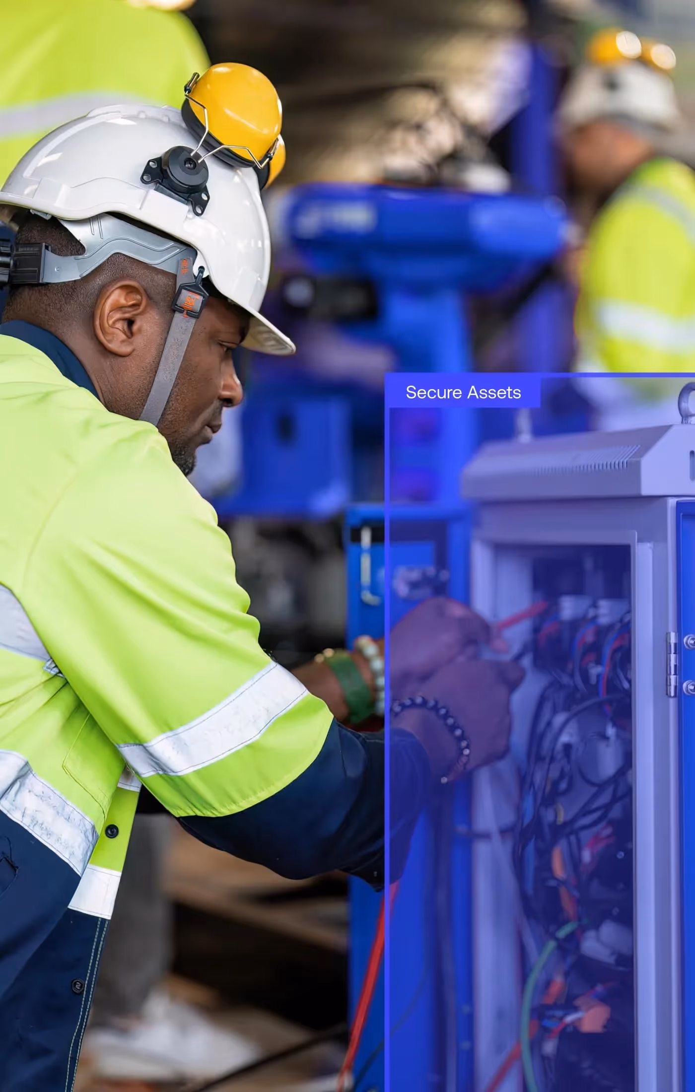 Worker in a high-visibility jacket and white helmet inspecting electrical equipment in an industrial setting.