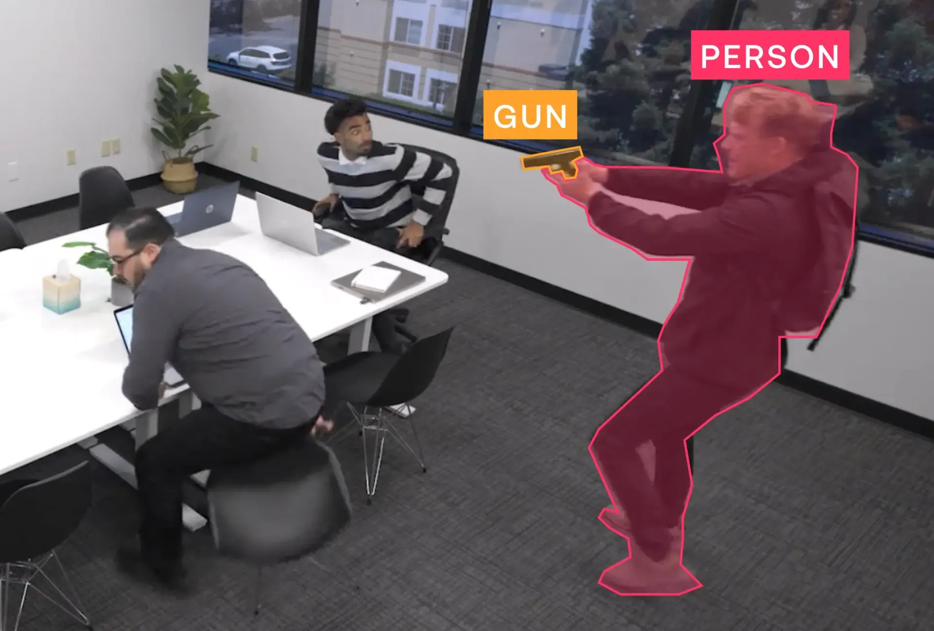 Person holding a gun detected in an office conference room with two seated men reacting.