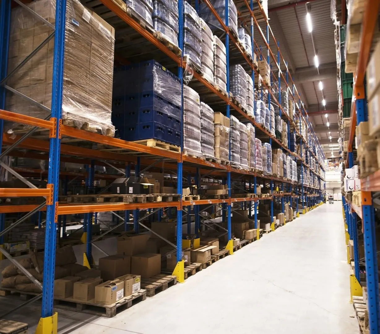 Großes Lager mit hohen Regalen, die mit Paletten und verpackten Kartons gefüllt sind.